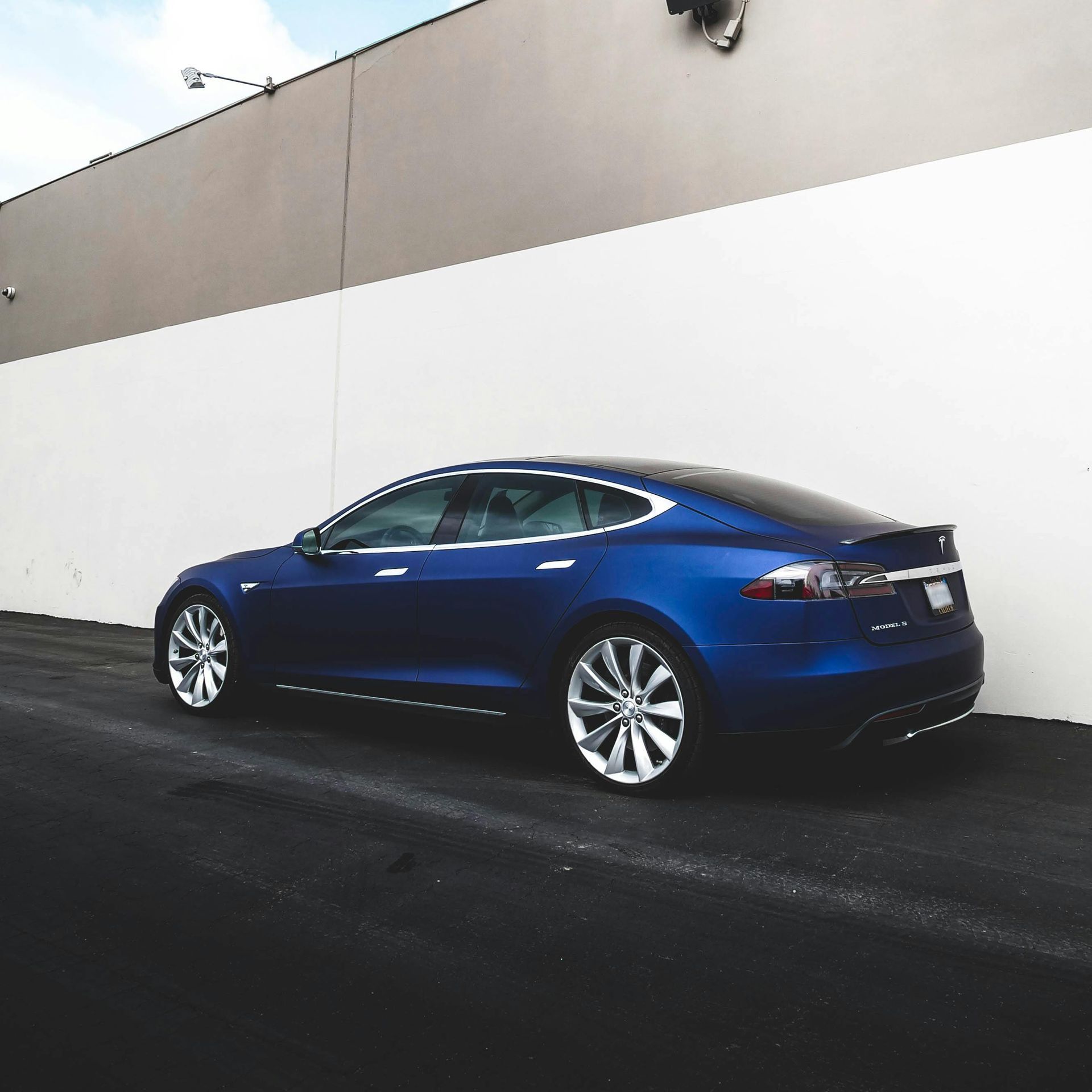 A blue tesla model s is parked in front of a white wall