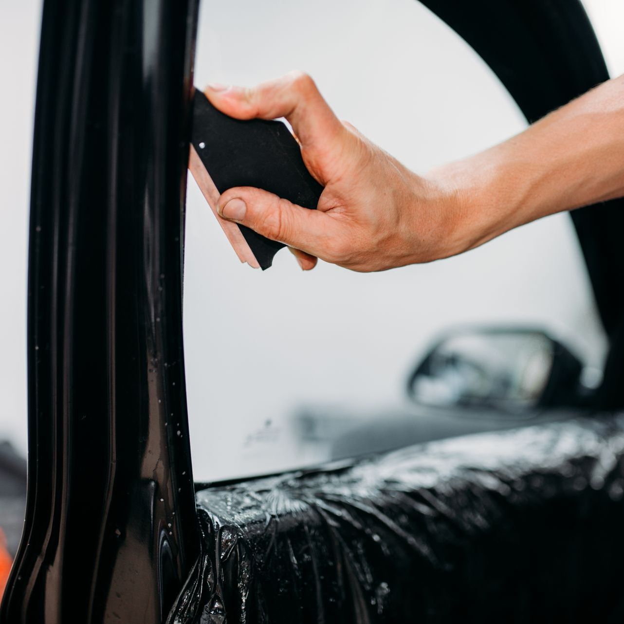 A person is wrapping a car window with black tape.