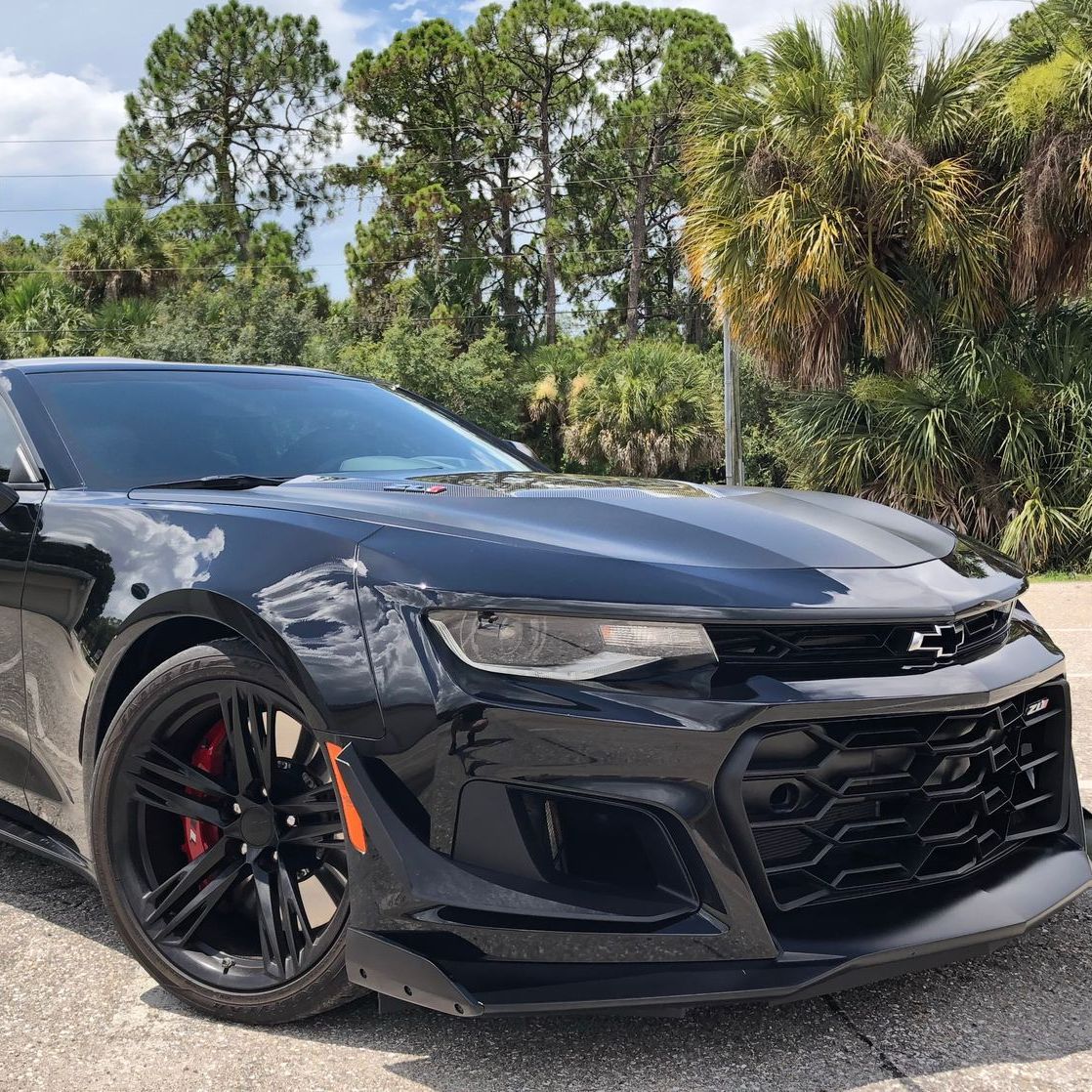 A black car is parked on the side of the road in front of trees.