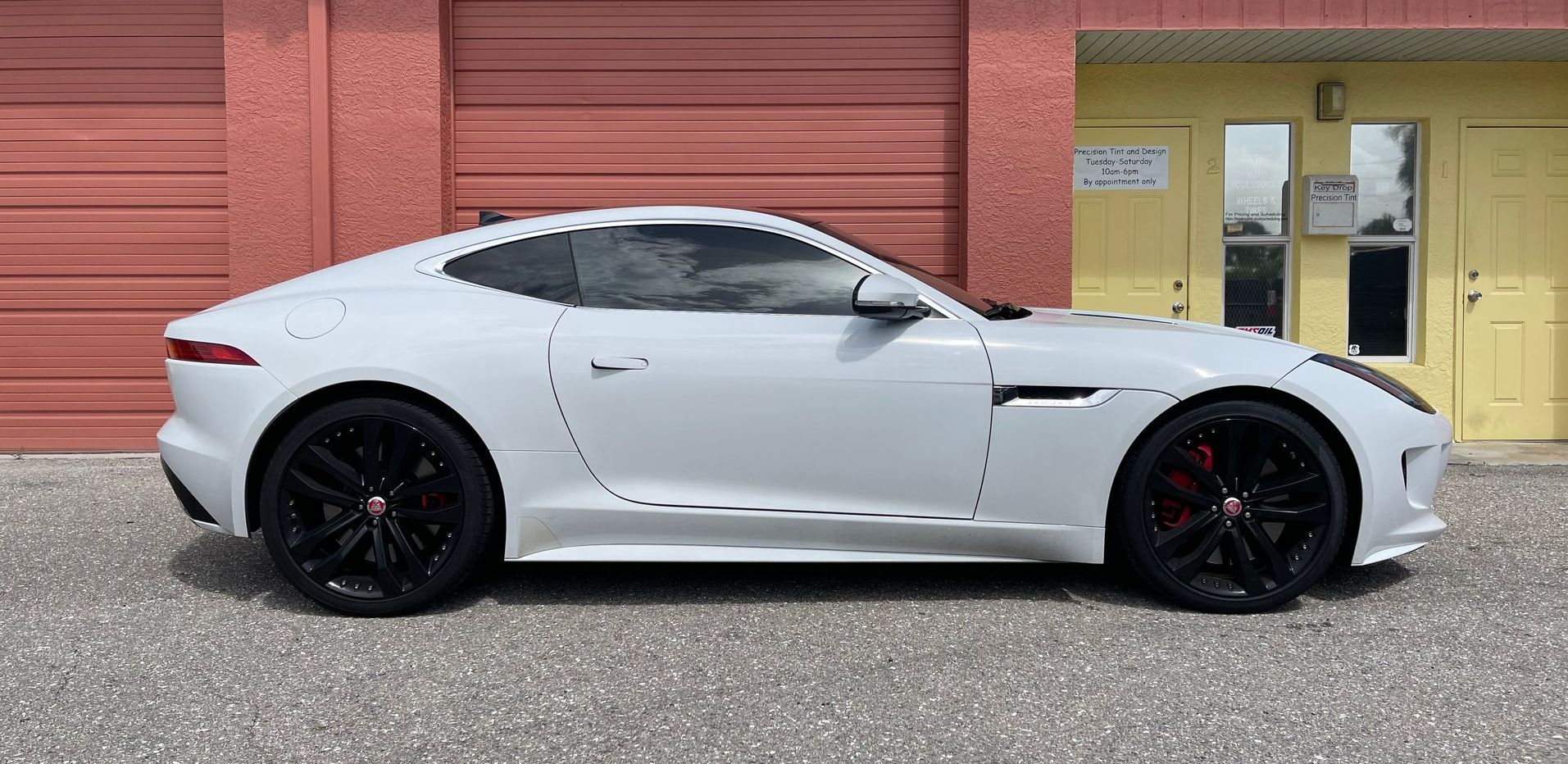 A white sports car is parked in front of a red garage door.