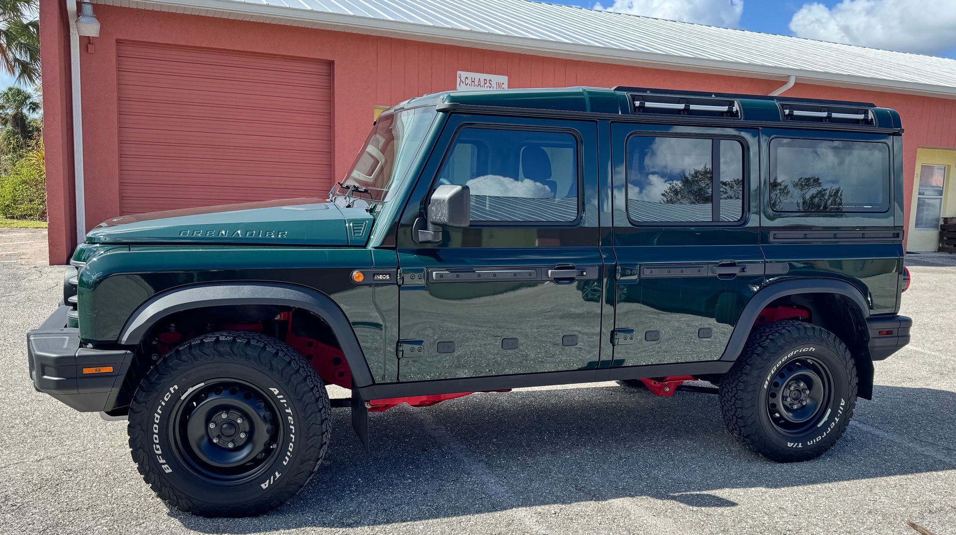 A green jeep is parked in front of a red building.