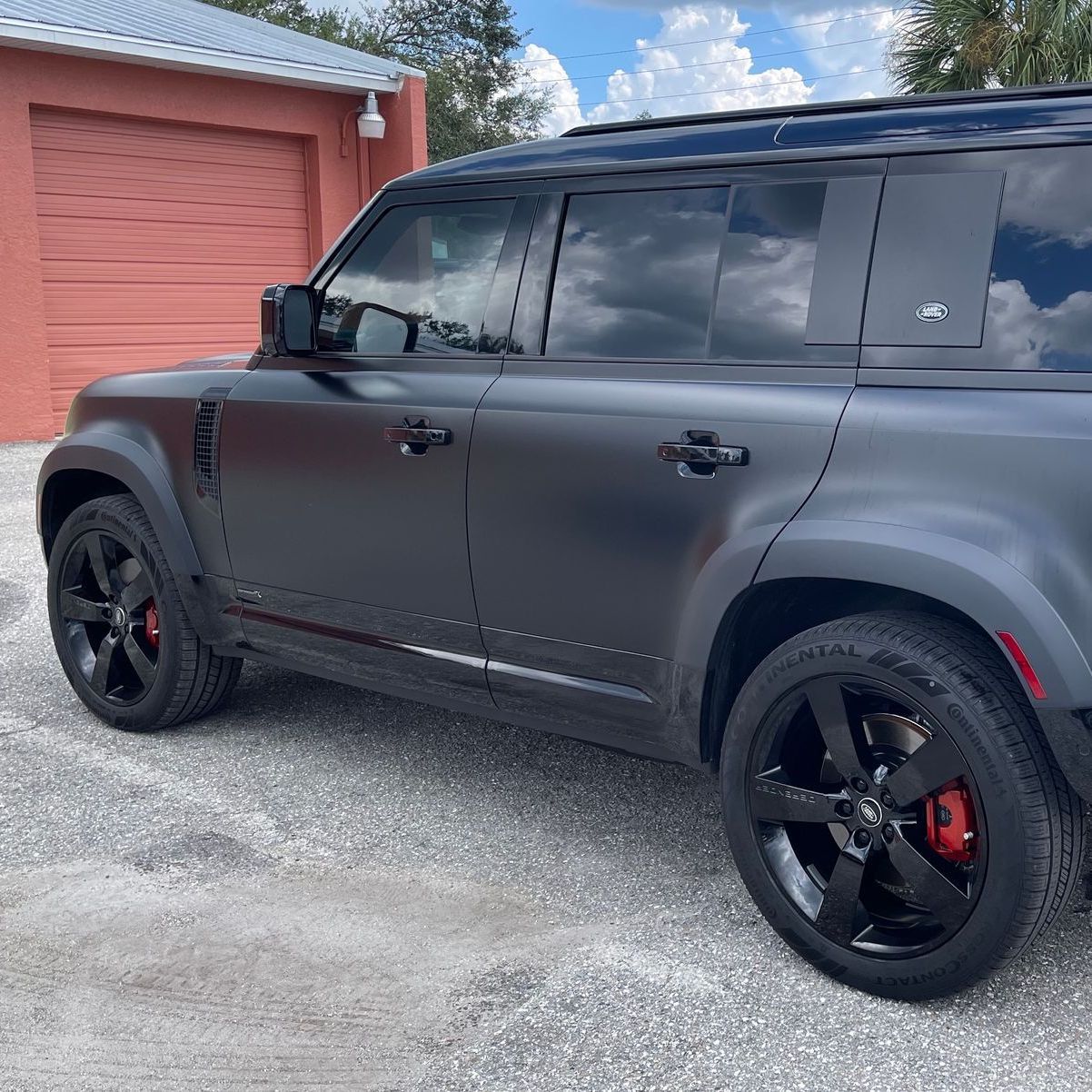 A black land rover defender is parked in front of a garage.