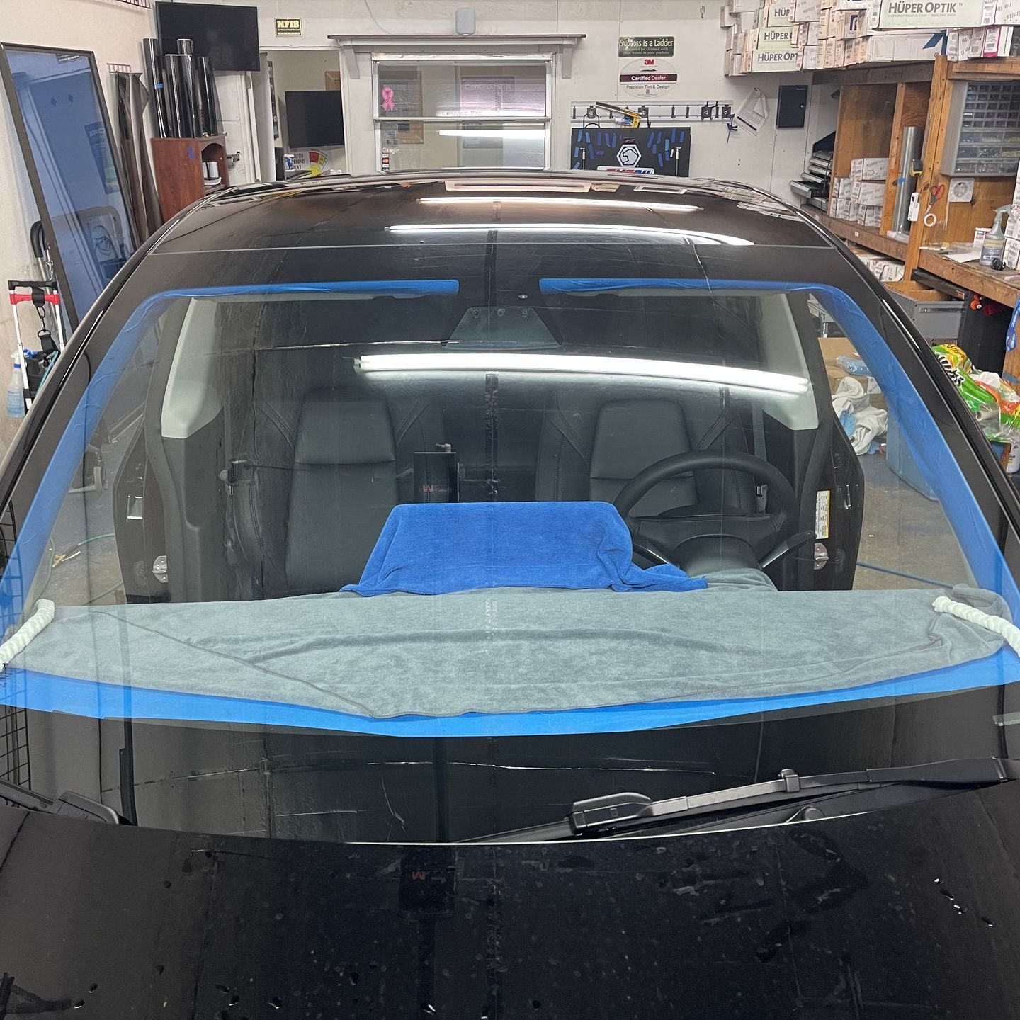 A black car with a blue towel on the windshield is sitting in a garage.