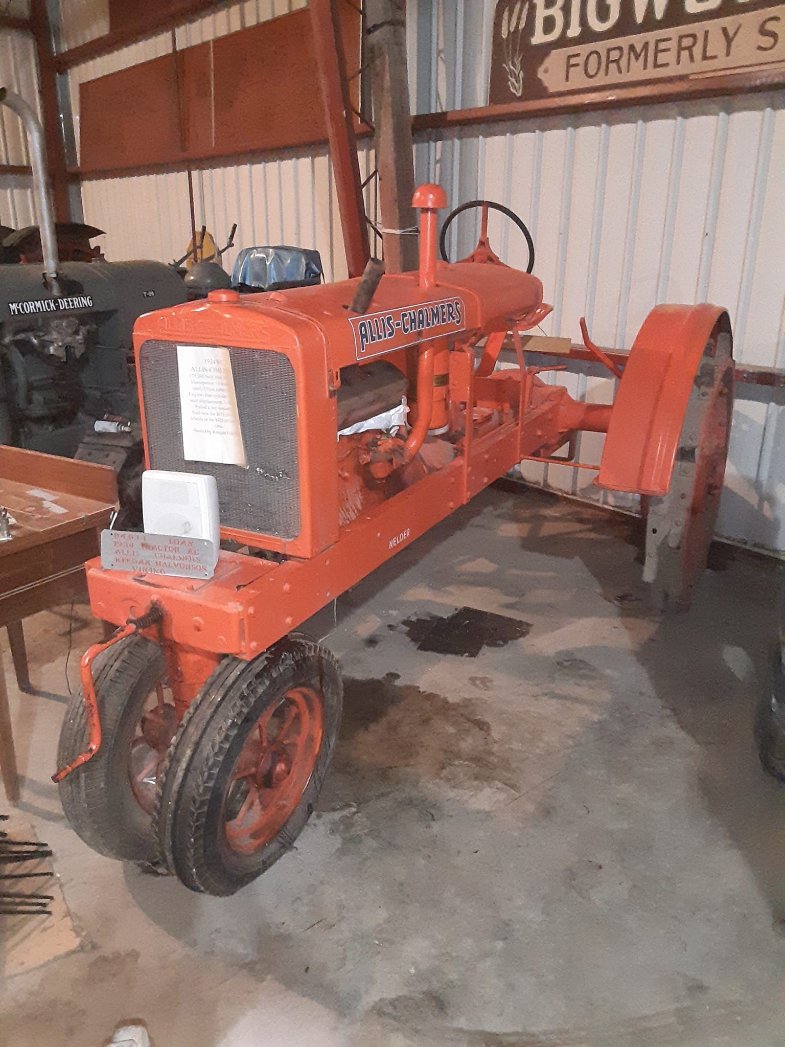 Orange vintage tractor inside a building, with black tires and steering wheel.