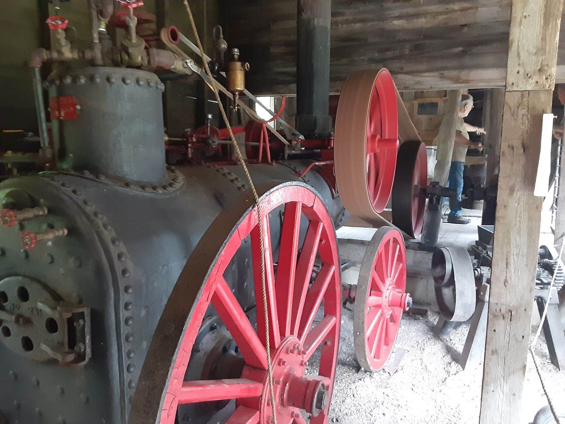 A large, vintage black steam engine with prominent red wheels sits inside a weathered wooden barn.