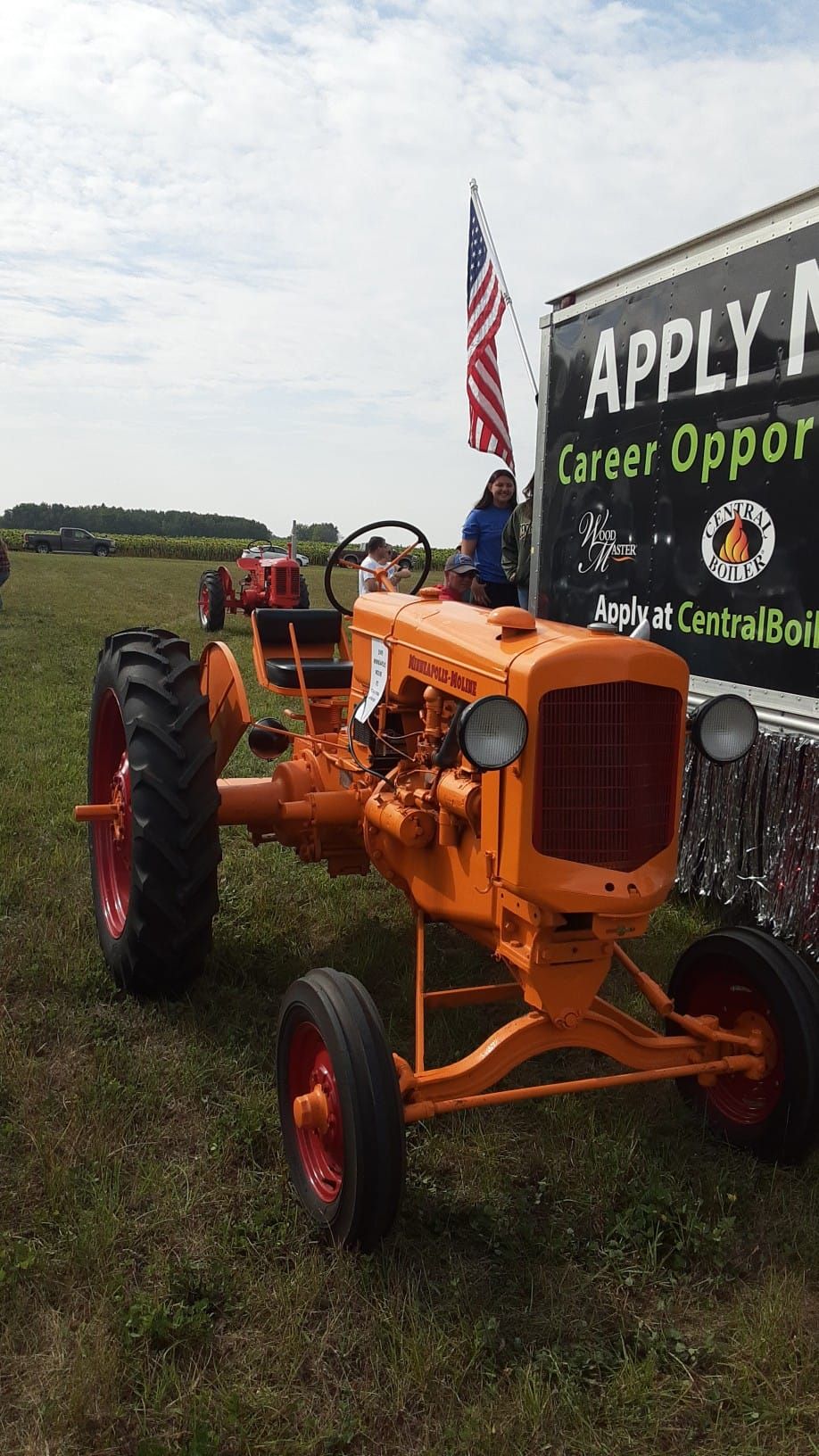 Orange vintage tractor with red wheels, displayed in a field, with American flag and sign.
