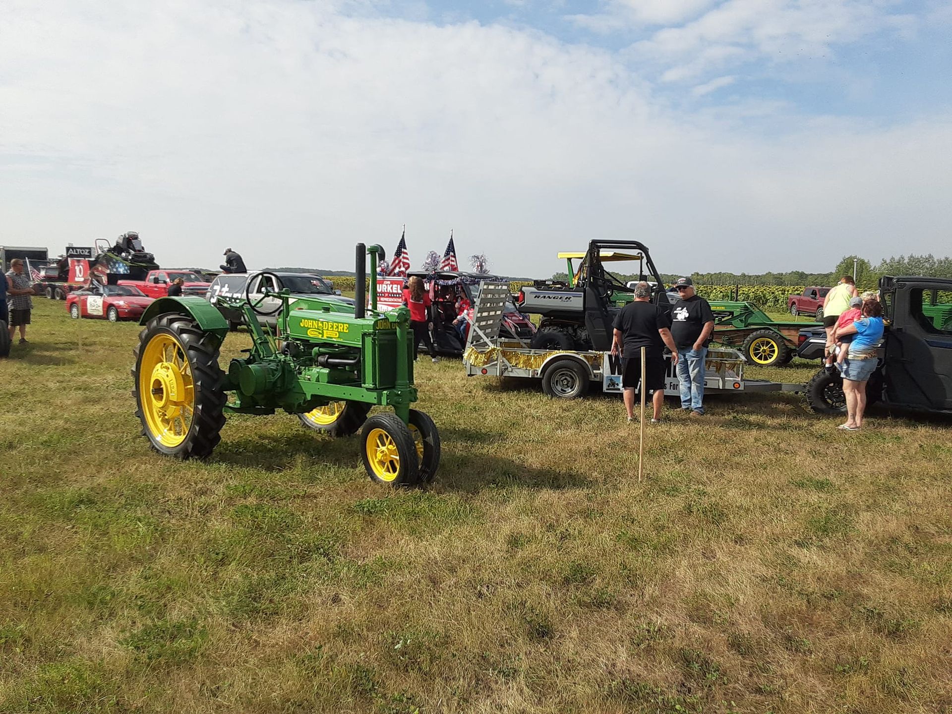 Green John Deere tractor on display at an outdoor event with other vehicles and people.