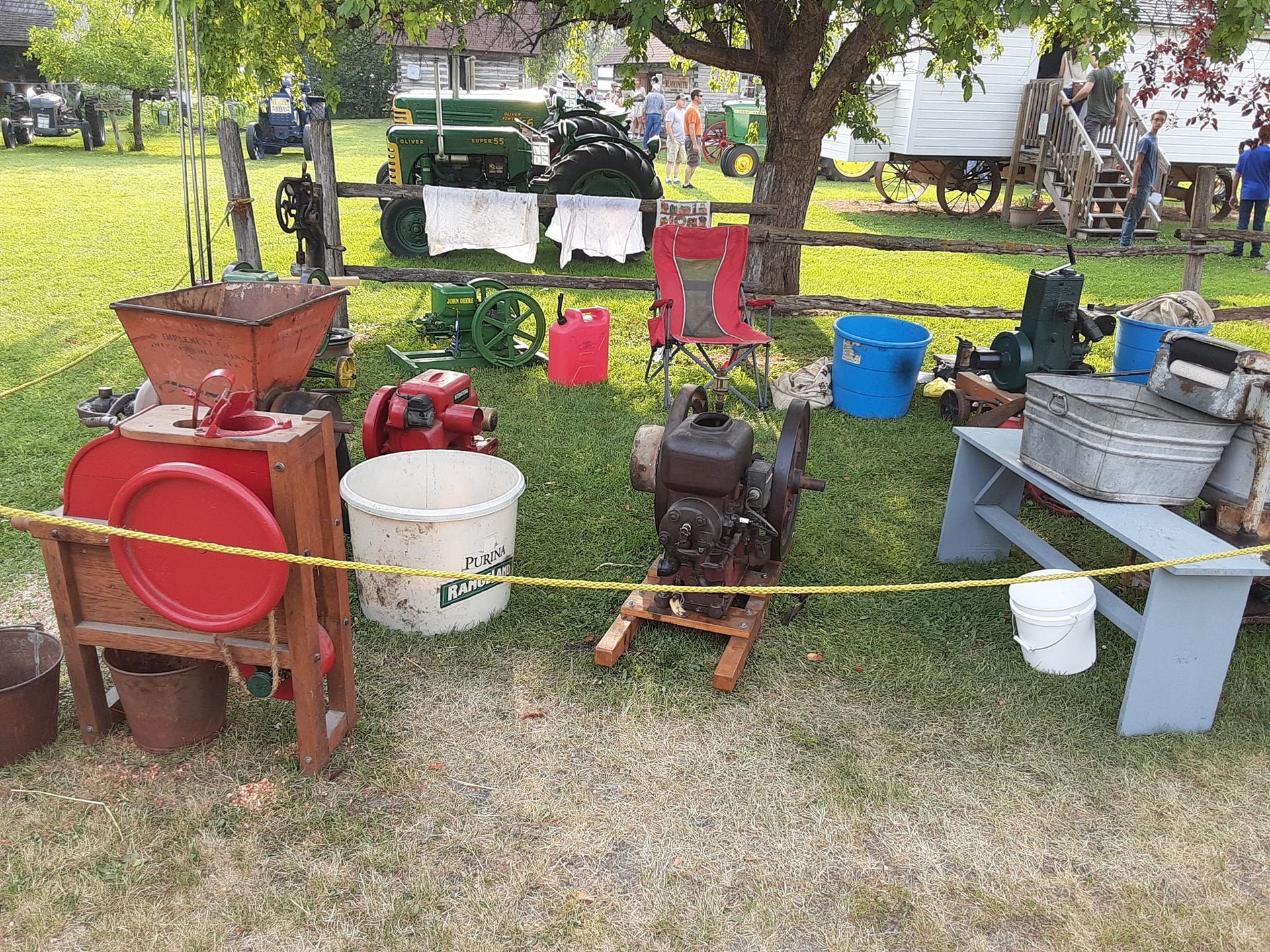 Outdoor display of antique farm equipment, including engines, grinders, and wash tubs on a grassy field.