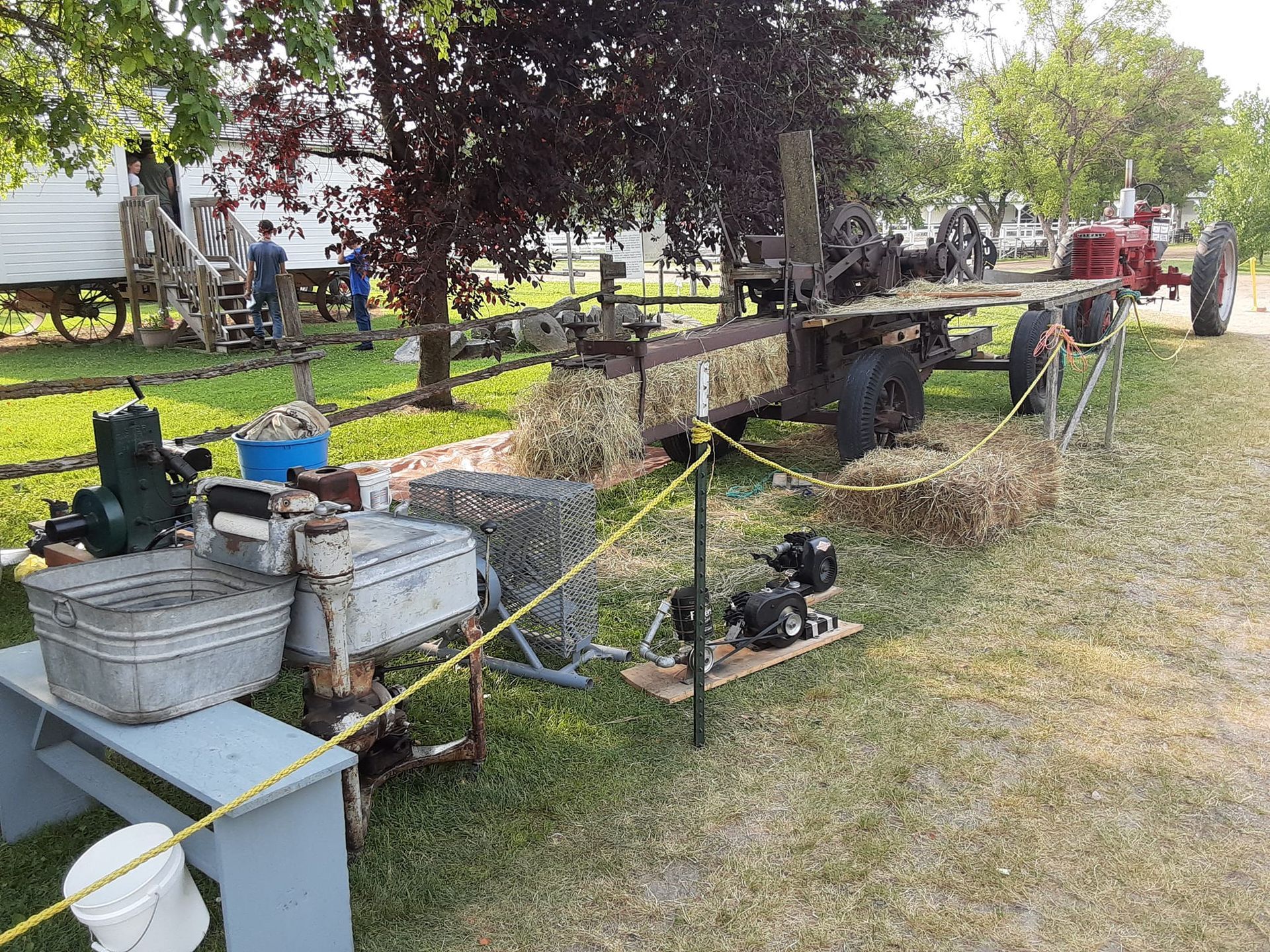 Display of antique farm machinery on a grassy field, including engines, a tractor, and hay bales.