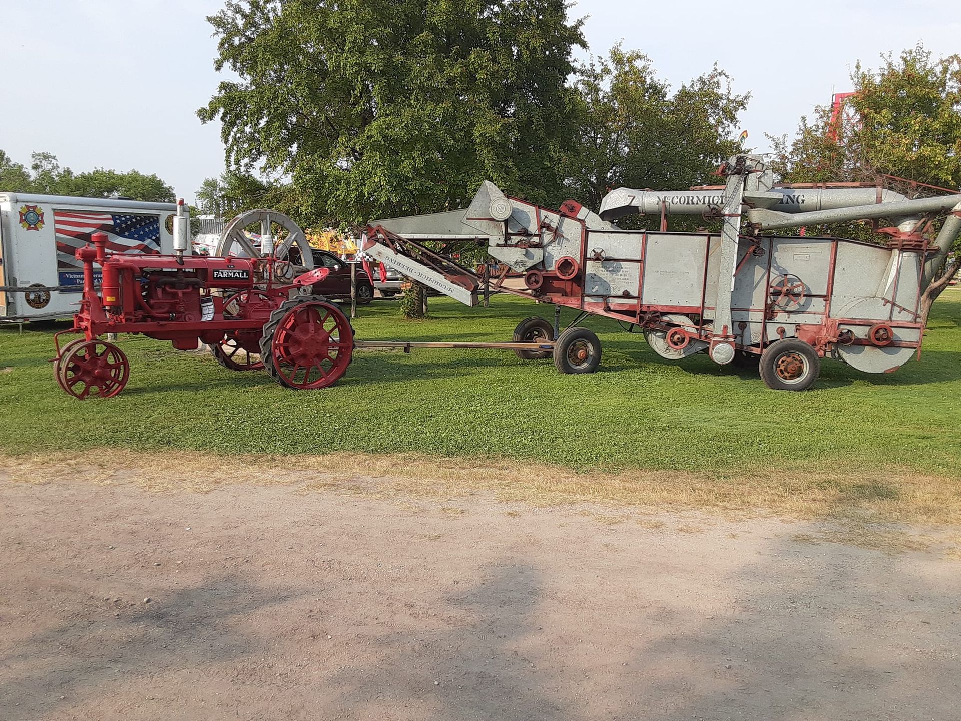 Red tractor pulling a vintage threshing machine on a grassy area.