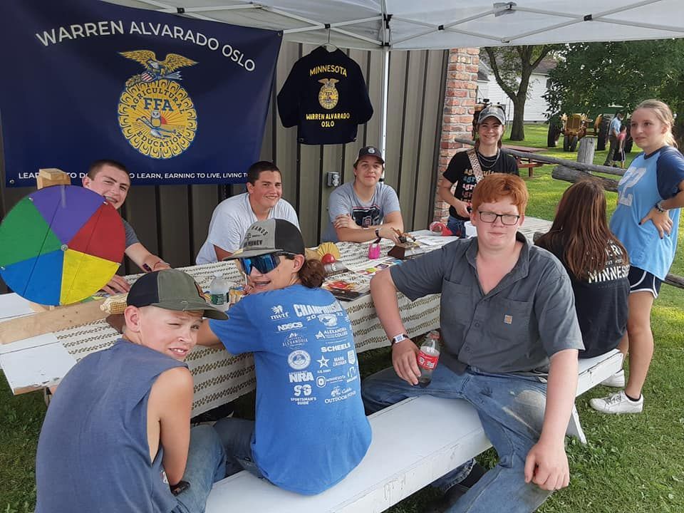 FFA members at a booth under a canopy, selling items. They are sitting at a table with a spinning prize wheel and snacks.