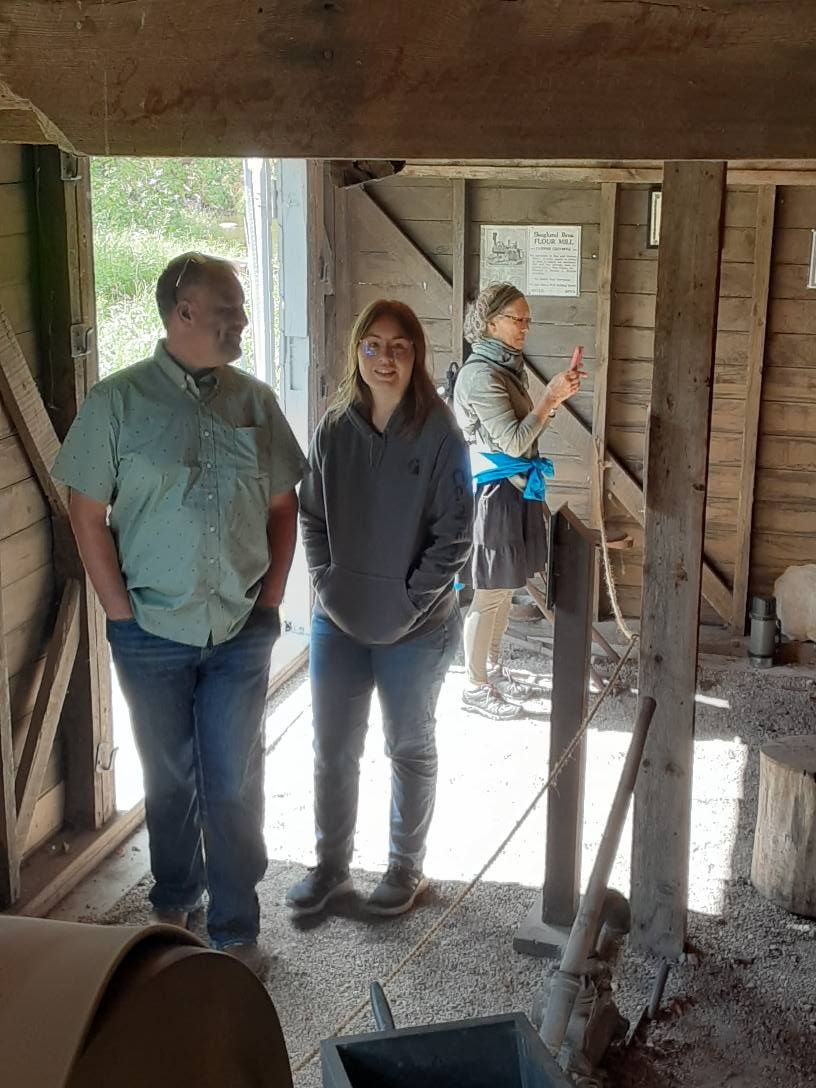 Three people inside a rustic wooden building, looking at something off-camera.