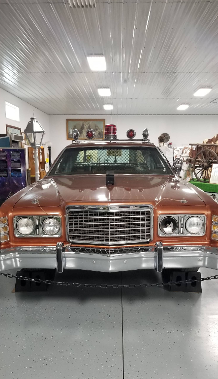 Brown vintage police car with lights on top and bumper. Inside a garage.