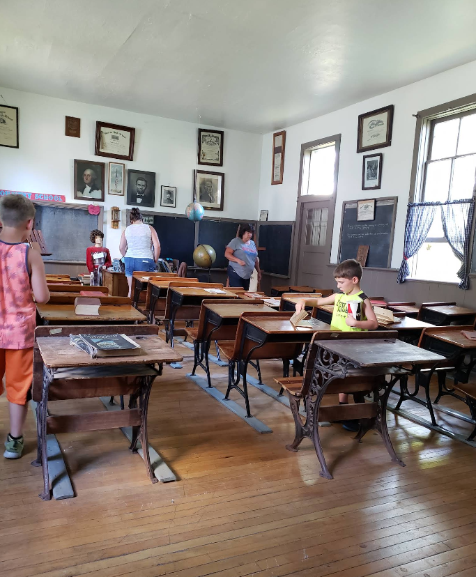 Old school classroom with desks, students, and historical items on walls.