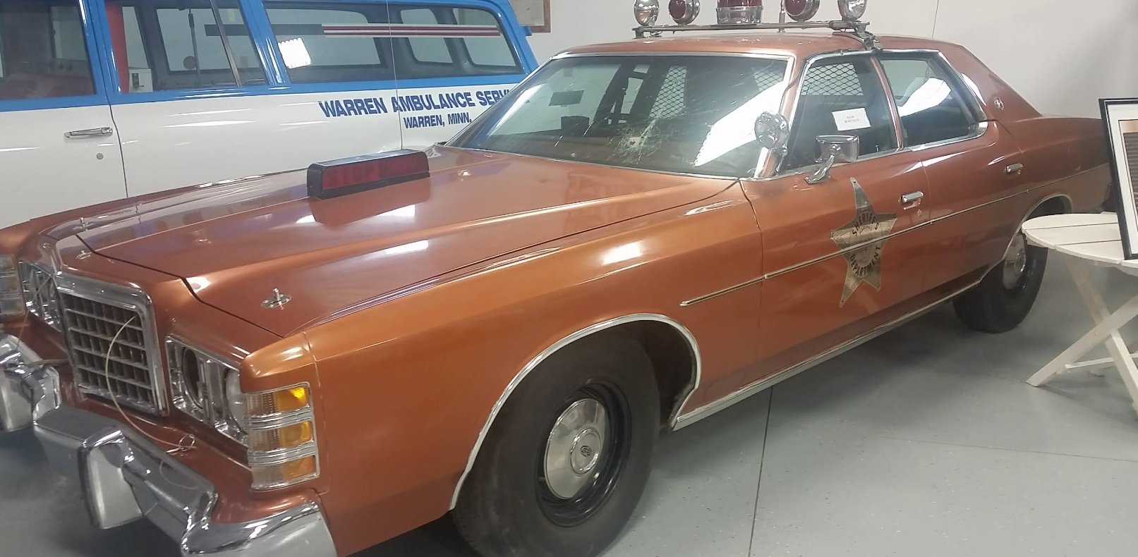 Brown vintage police car with lights and insignia on display.