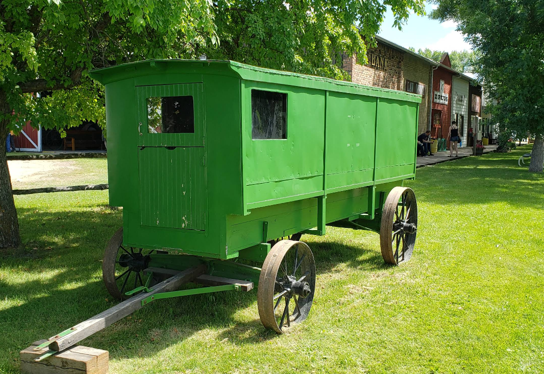 Green wooden wagon on wheels with two windows, parked on grass.