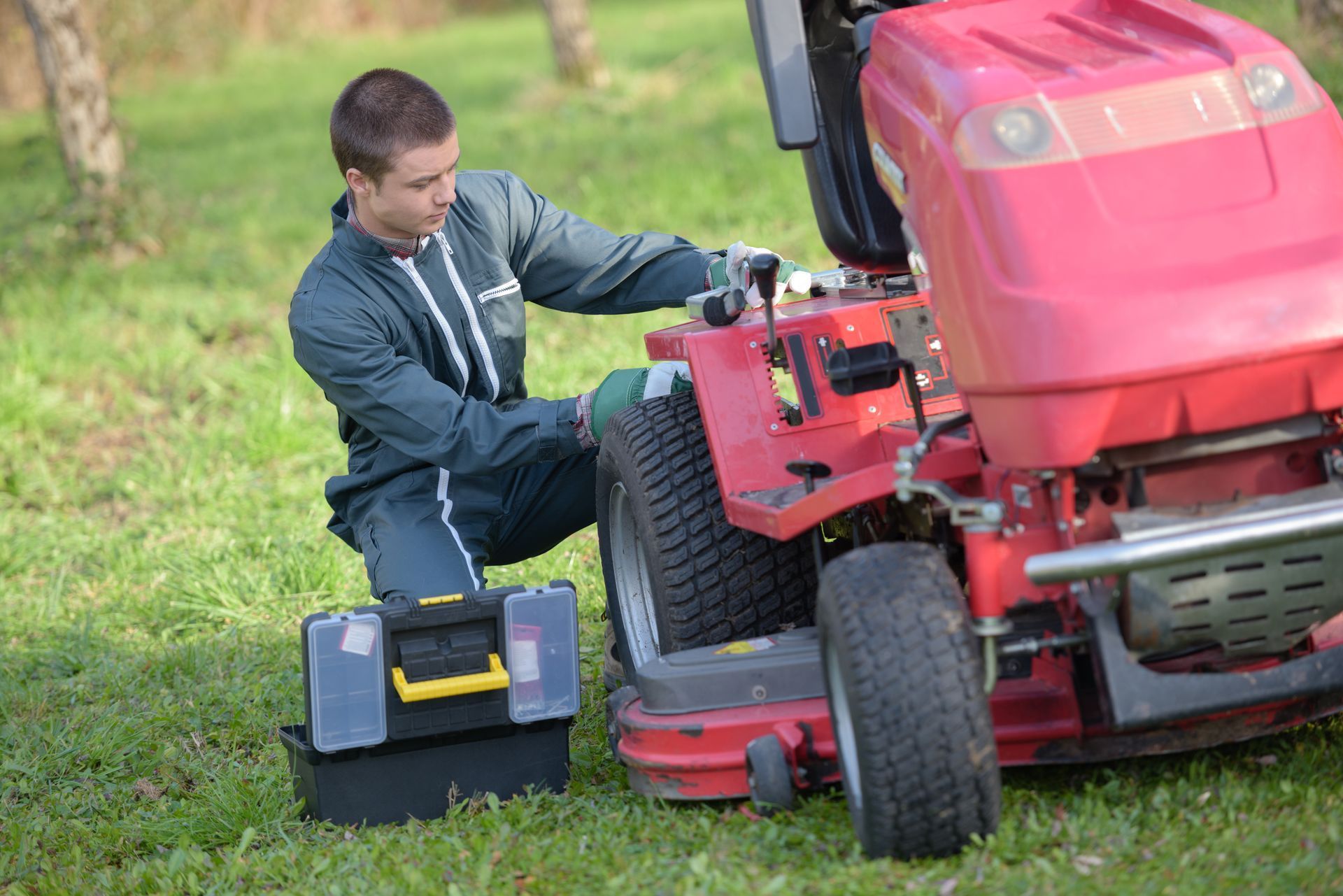 A man is kneeling down to fix a lawn mower. — Somerset Ride-On Mower Repairs In Kilcoy, QLD