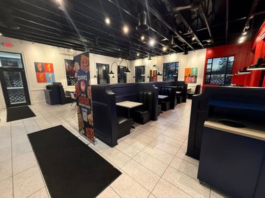 Empty restaurant dining area with dark booths, red walls, and tiled floor under ceiling lights
