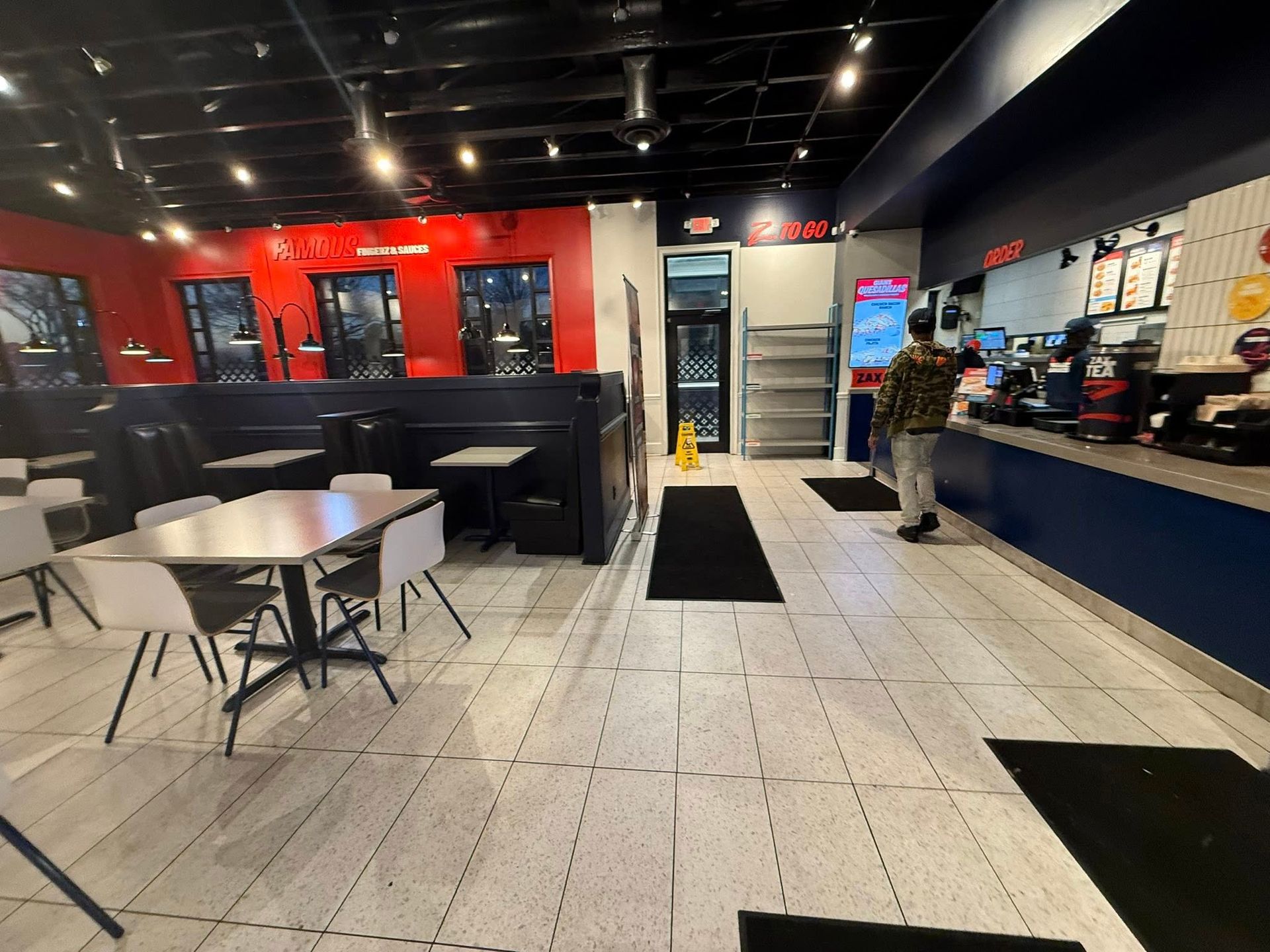 Modern cafe interior with red walls, tables, stools, and a person standing near the counter