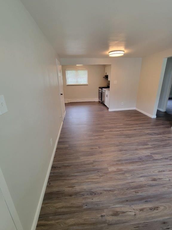 A living room with hardwood floors and a kitchen in the background.