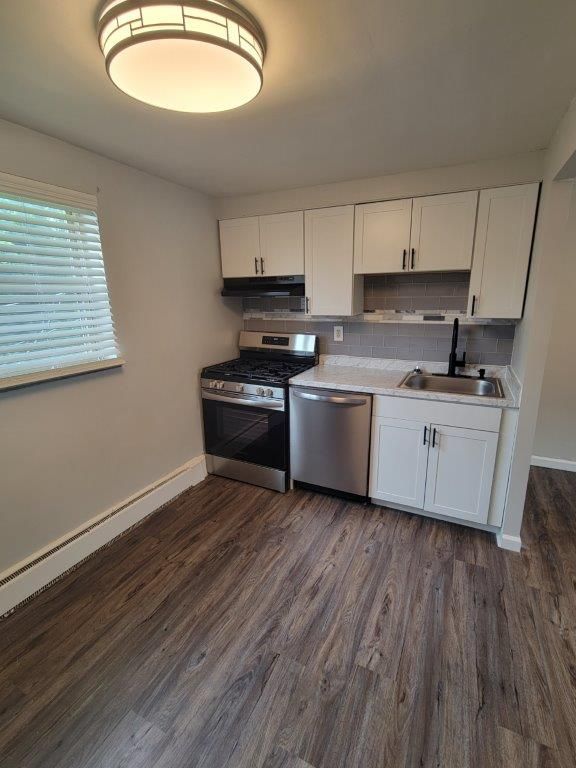 A kitchen with white cabinets , a stove , a sink , and a window.