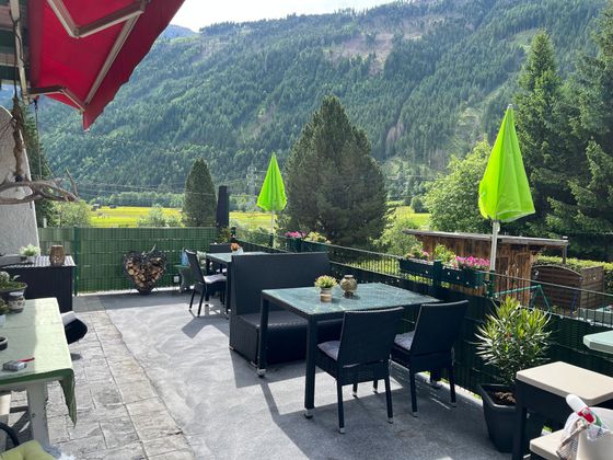Een terras met tafels, stoelen, parasols en uitzicht op de bergen.