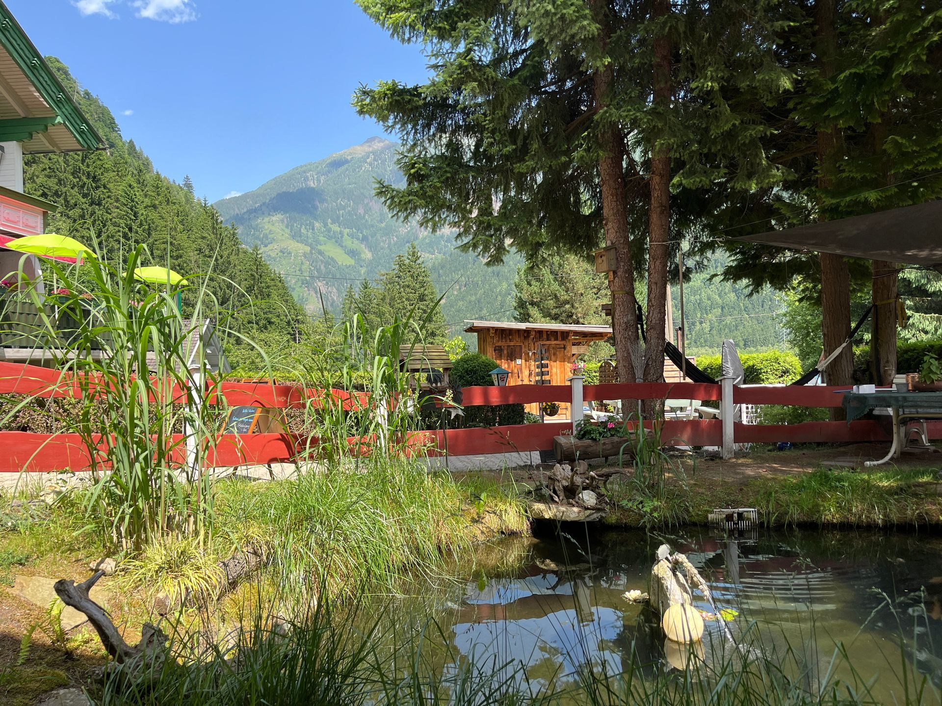 Vijver met groen en rood hekwerk, bomen en bergen op de achtergrond op een zonnige dag.