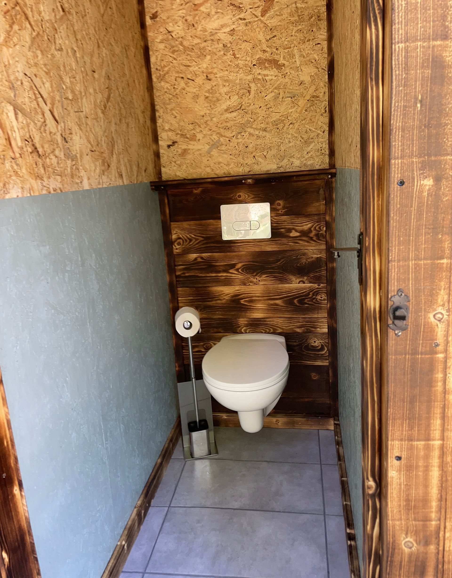 Een toilet in een badkamer met een houten wand