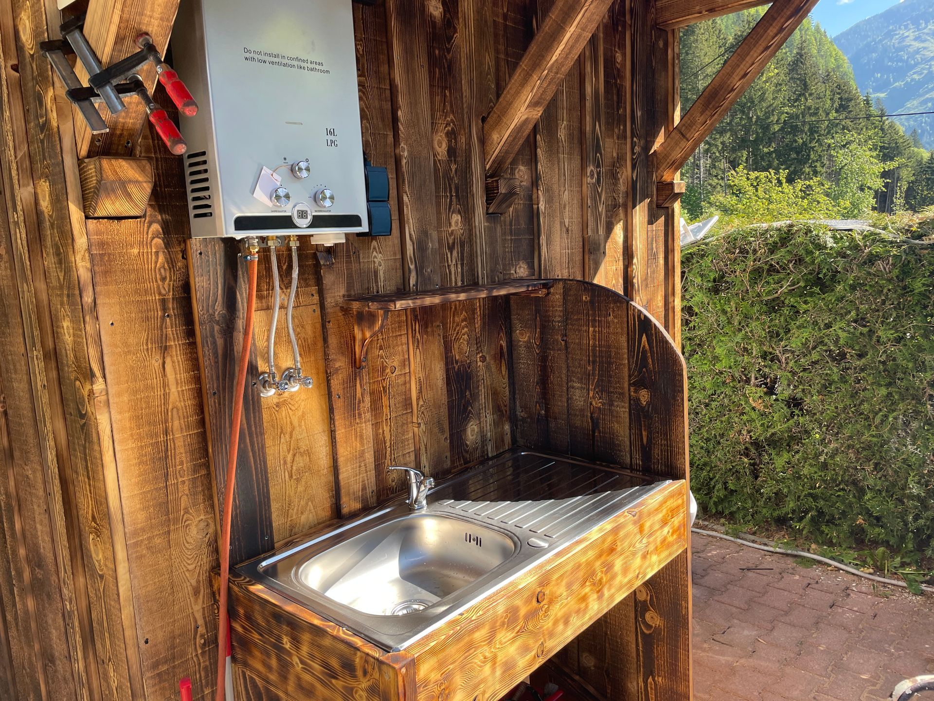 Een houten schuurtje met een gootsteen en een gaskachel eraan vast.