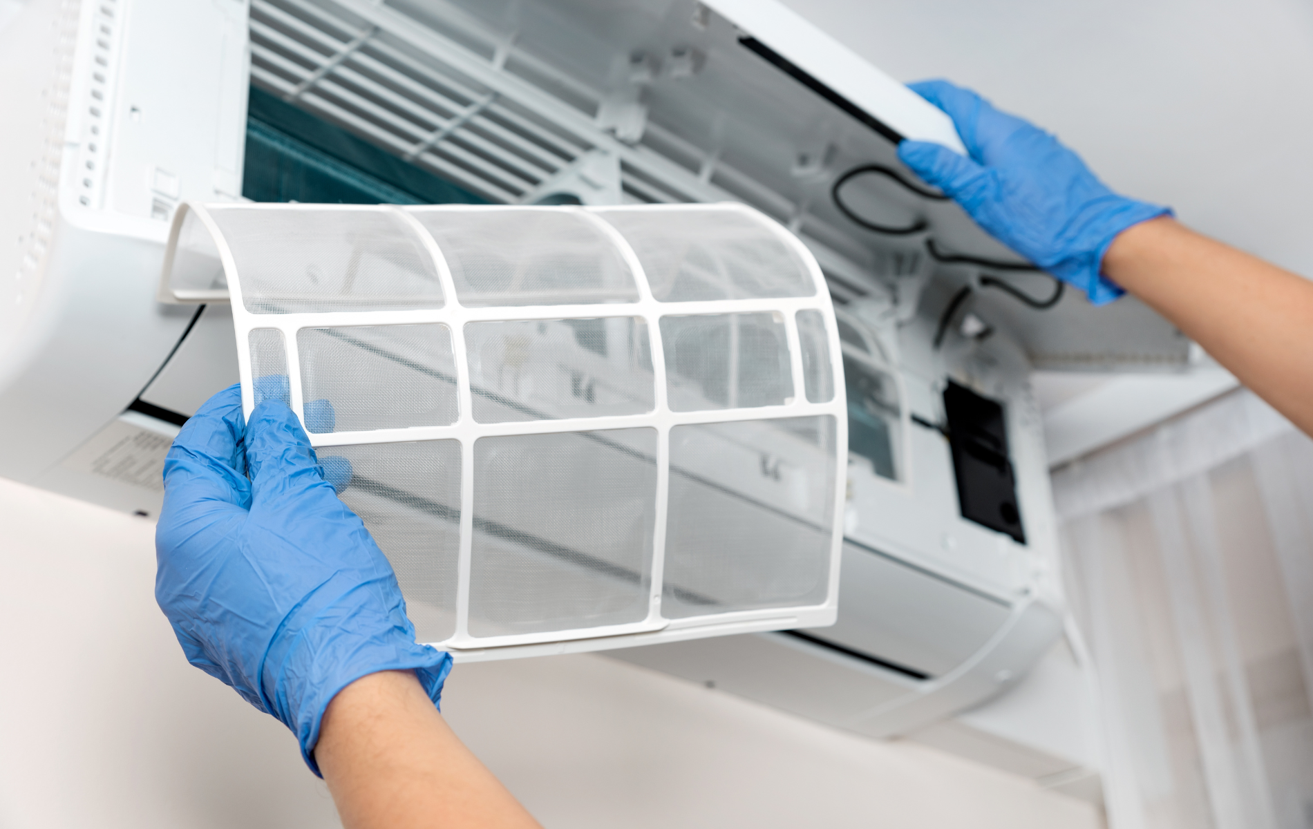 A person wearing blue gloves is cleaning an air conditioner.