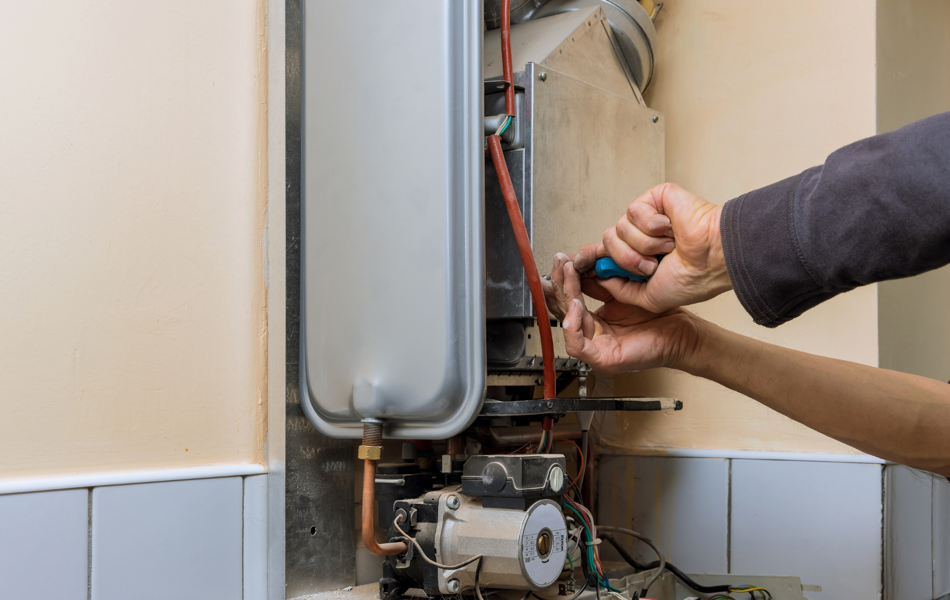 A person is fixing a boiler with a screwdriver.