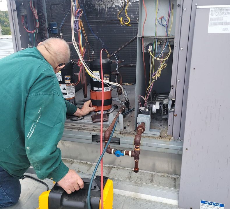 A man in a green jacket is working on an air conditioner.