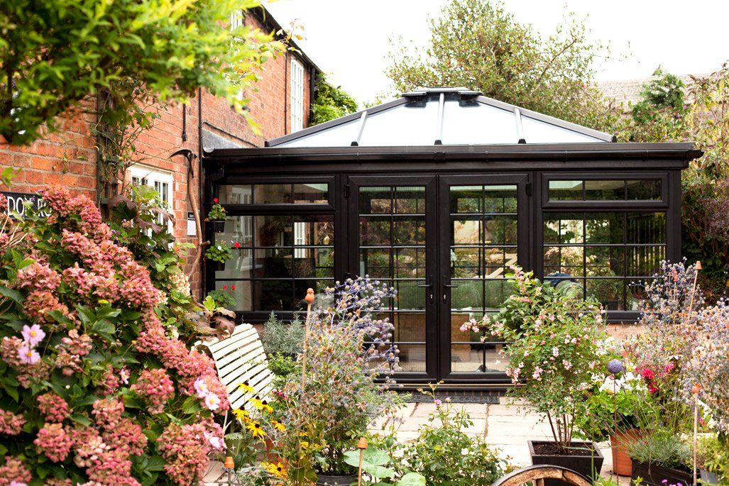 A garden with flowers and a brown conservatory in the background