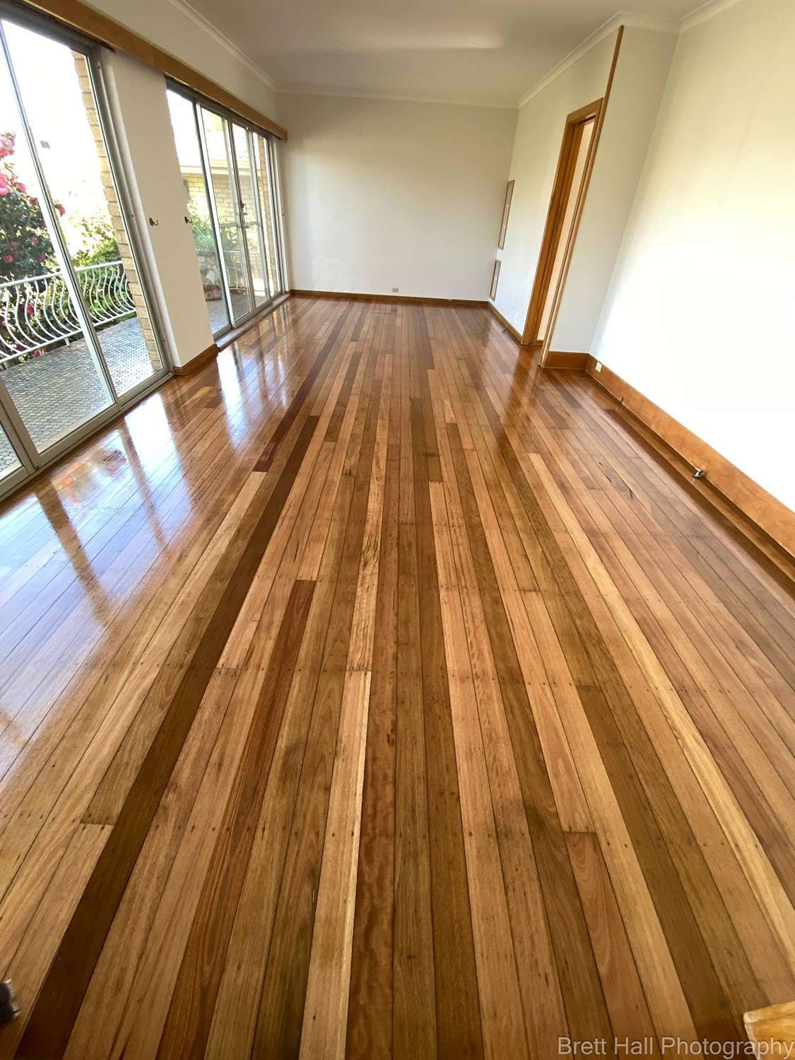 A Large Empty Room With A Polished Wooden Floor And Lots Of Windows — Brett Hall Floorsanding in Port Macquarie, NSW