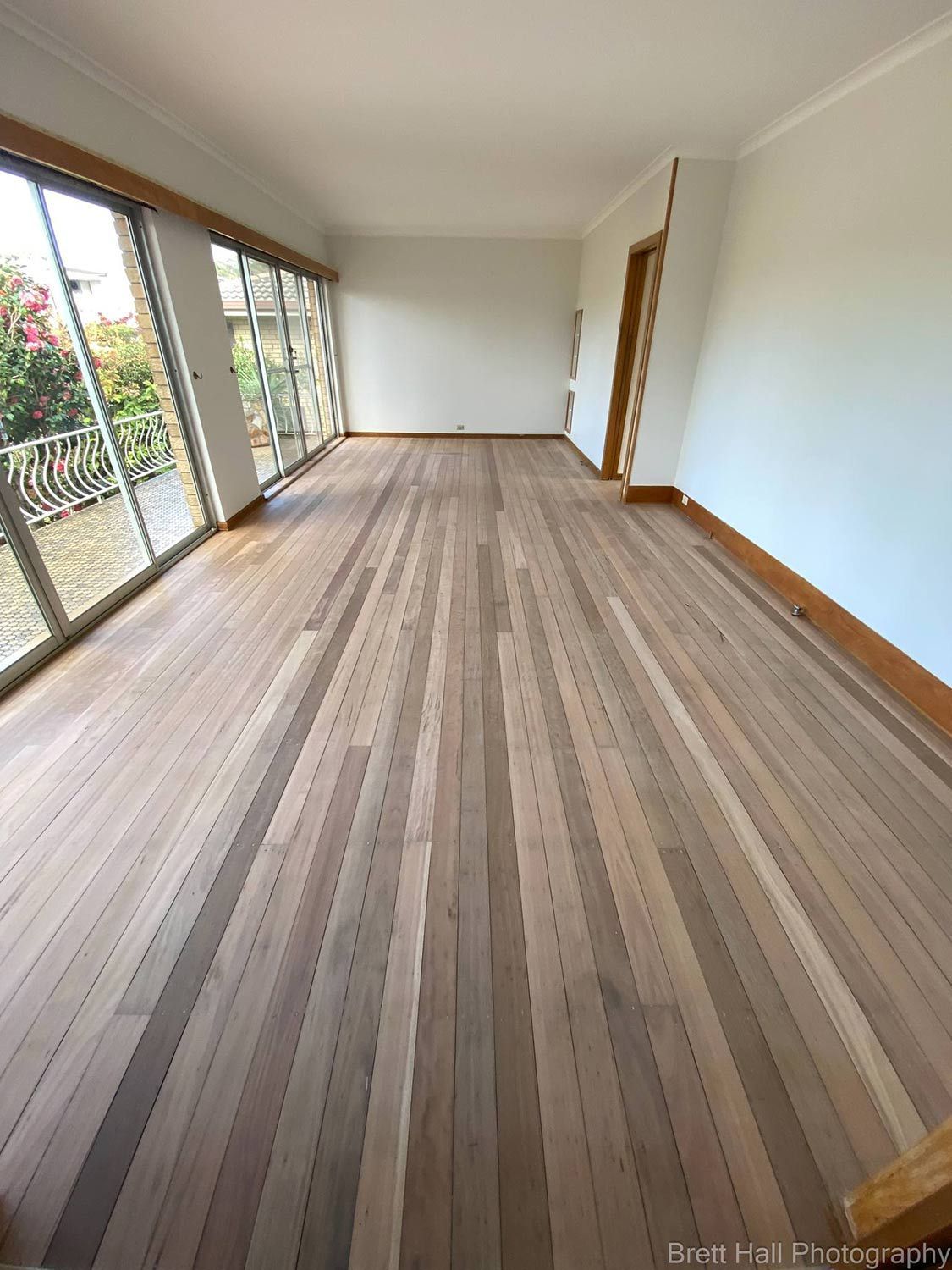 A Large Empty Room With A Sanded Wooden Floor And Sliding Glass Doors — Brett Hall Floorsanding in Port Macquarie, NSW