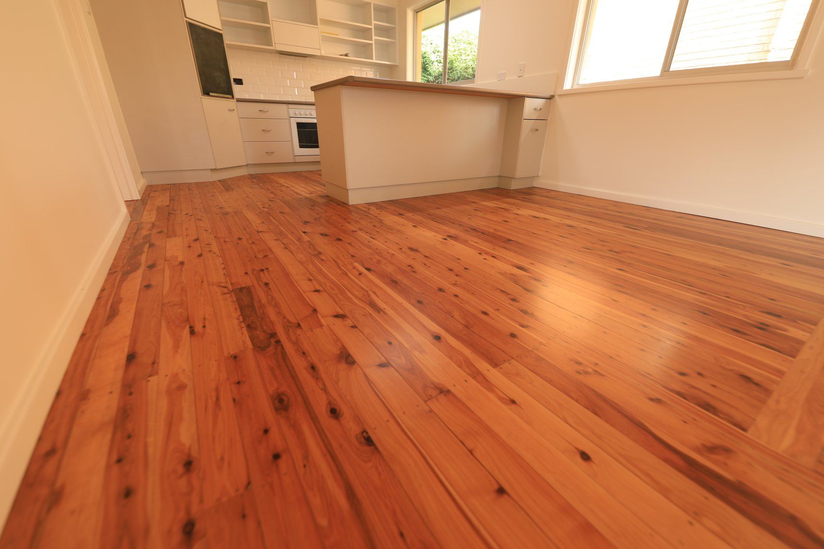 An Empty Room With A Wooden Floor And A Kitchen In The Background — Brett Hall Floorsanding in Port Macquarie, NSW