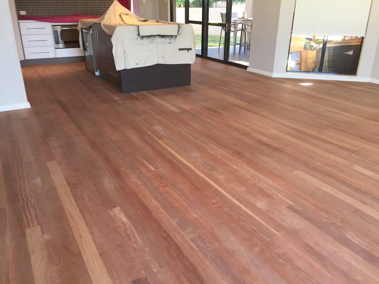 A Wooden Floor In A Living Room With A Kitchen In The Background — Brett Hall Floorsanding in Laurieton, NSW