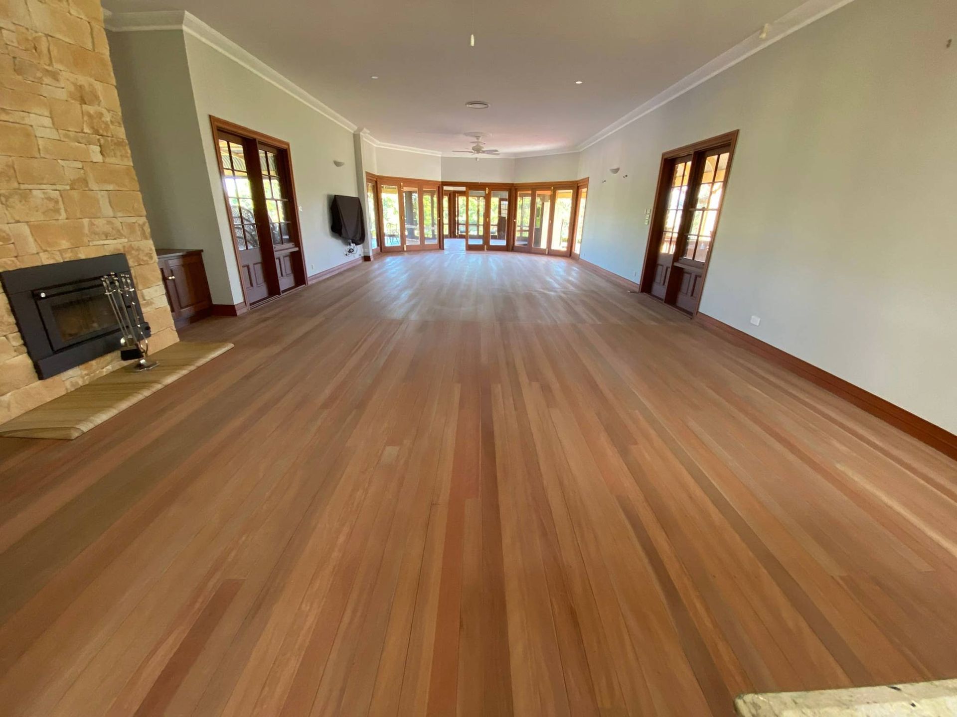 A Large Empty Room With Hardwood Floors And A Fireplace — Brett Hall Floorsanding in Port Macquarie, NSW