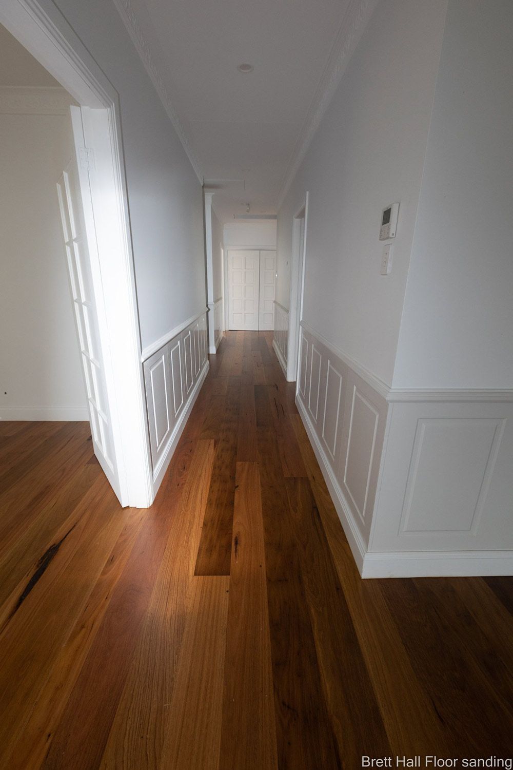 A Long Hallway With Polished Wooden Floors And White Walls — Brett Hall Floorsanding in Kempsey, NSW