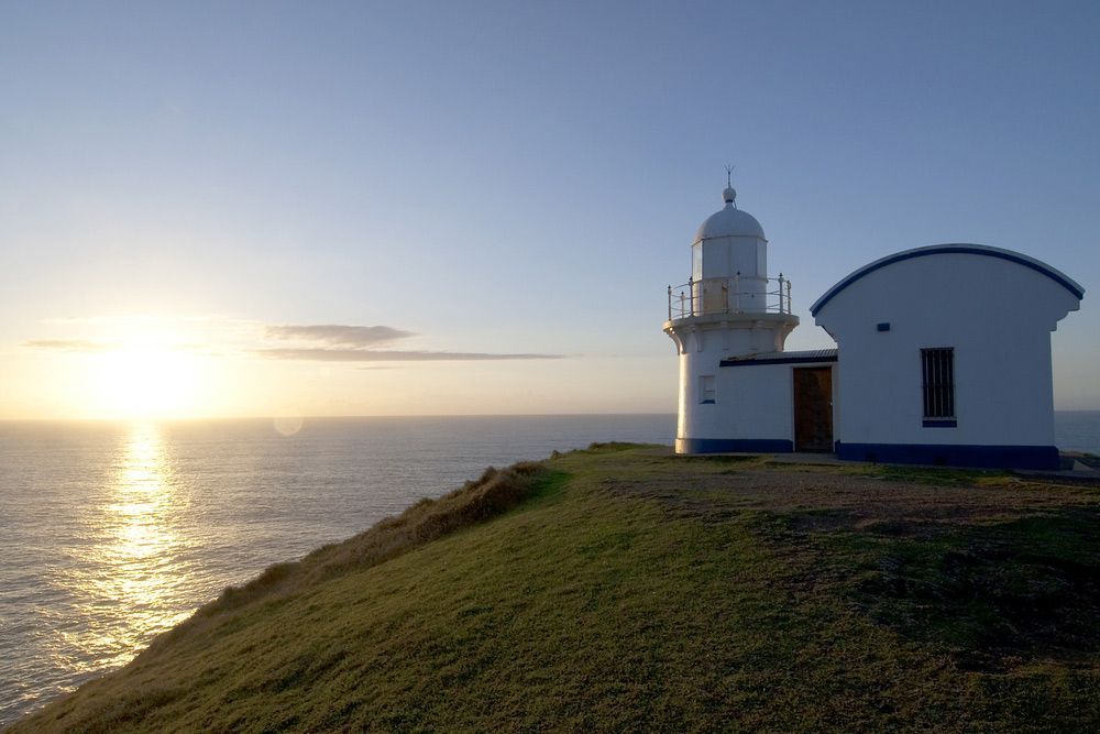 A Lighthouse On A Cliff Overlooking The Ocean At Sunset — Brett Hall Floorsanding in Port Macquarie, NSW