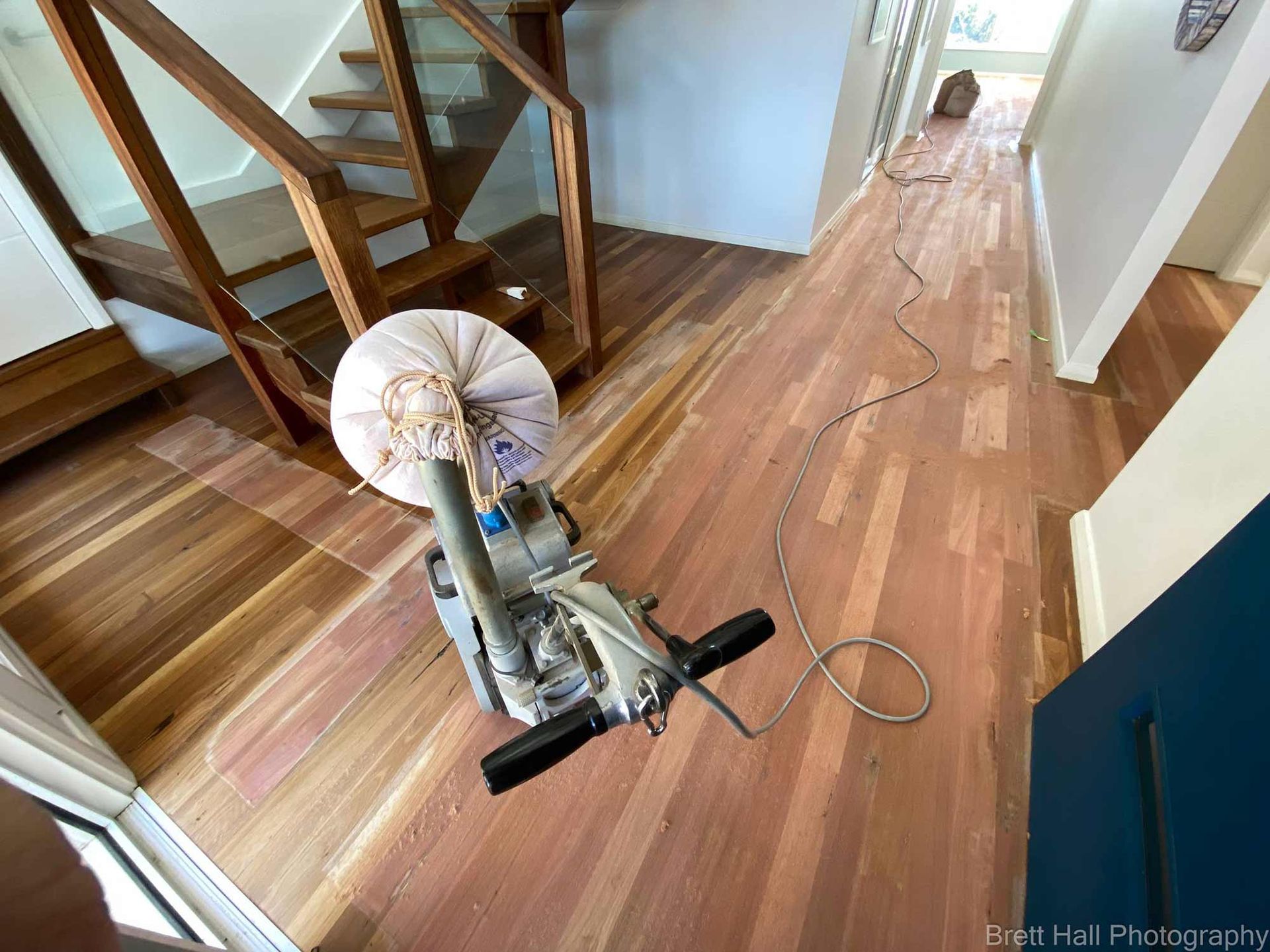 A Machine Is Sitting On A Wooden Floor In A Hallway Next To A Staircase — Brett Hall Floorsanding in Port Macquarie, NSW