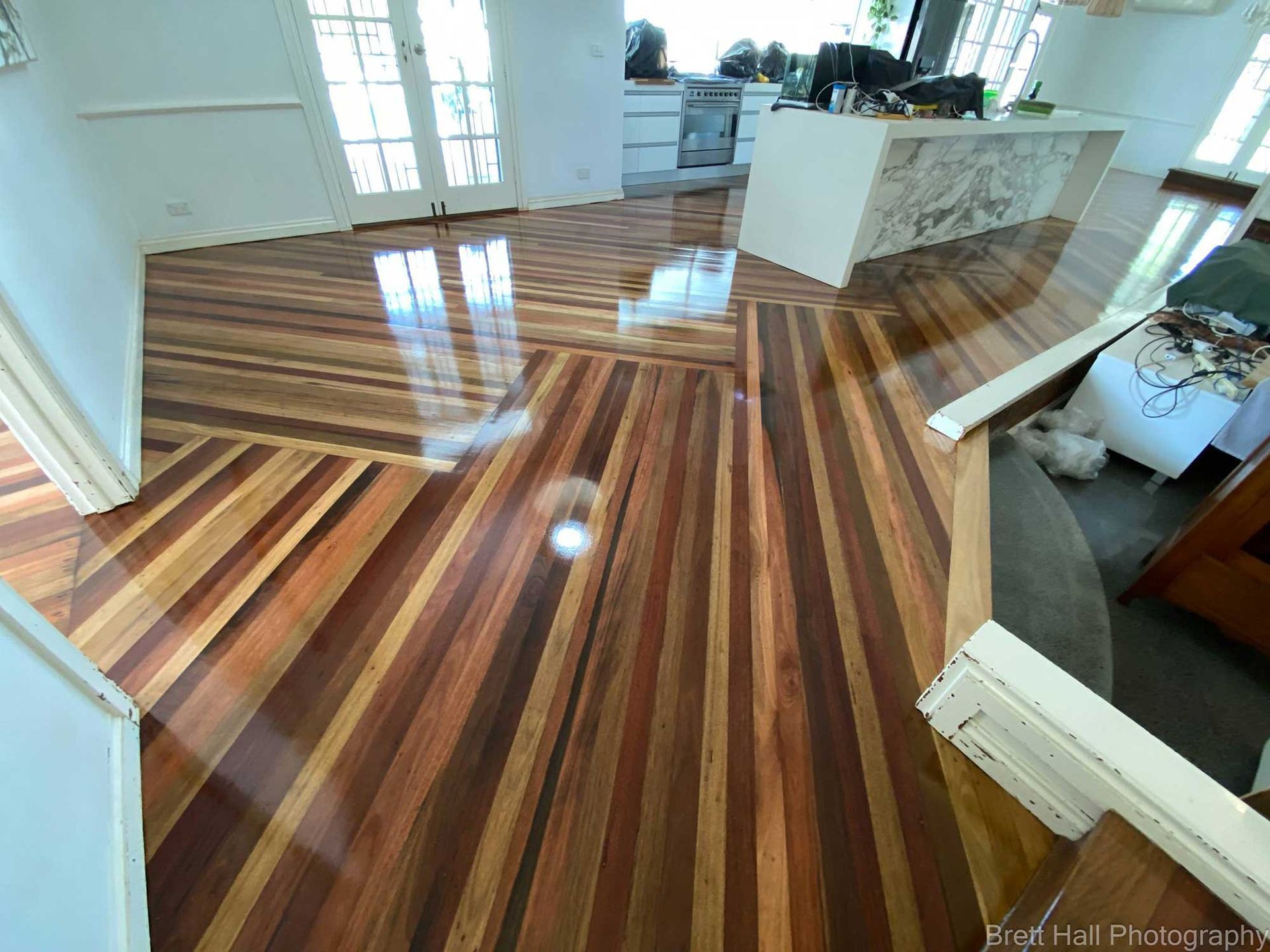 A Wooden Floor In A Living Room With A Kitchen In The Background — Brett Hall Floorsanding in Port Macquarie, NSW