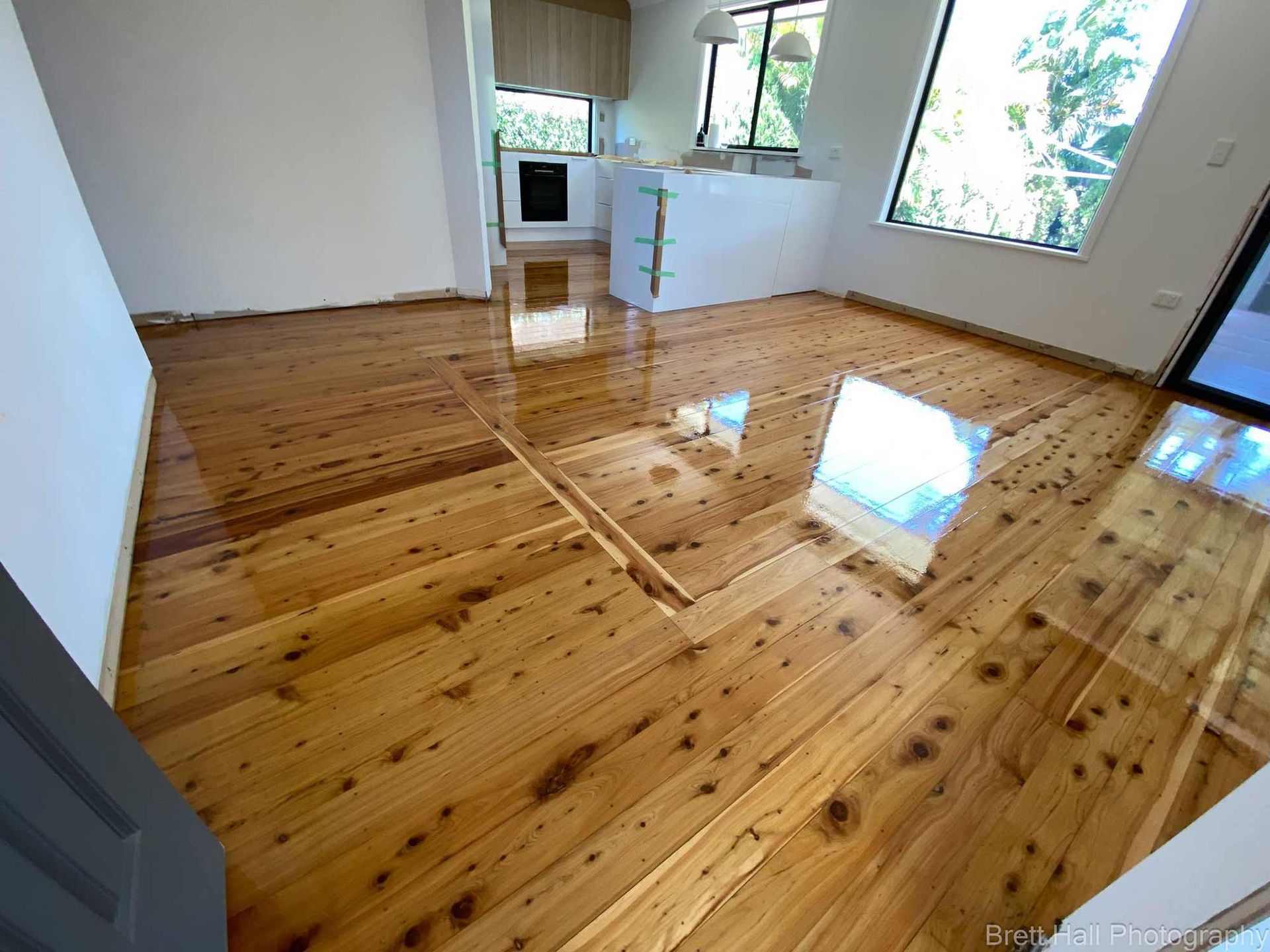 A Living Room With A Wooden Floor And A Kitchen In The Background — Brett Hall Floorsanding in Port Macquarie, NSW