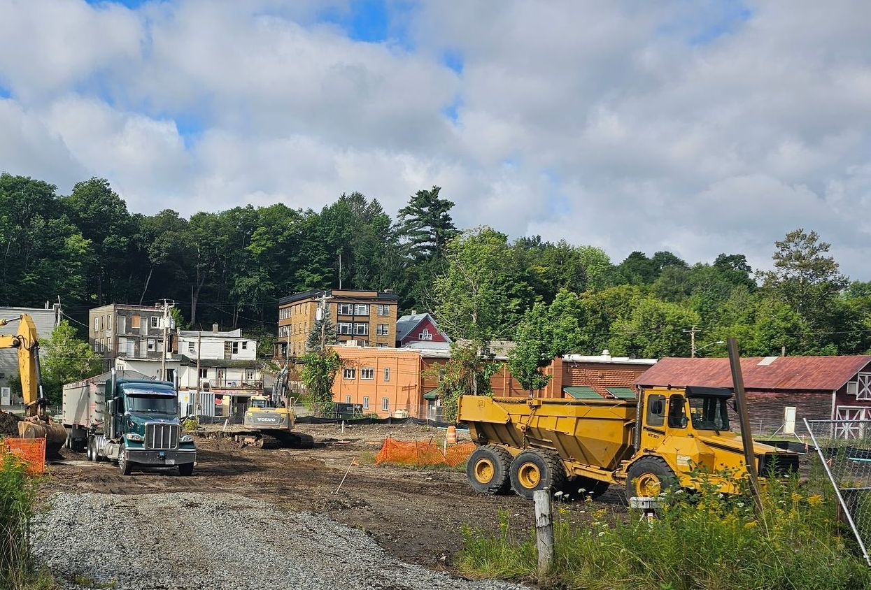 Construction site with heavy machinery removing buildings, sky and trees in the background.