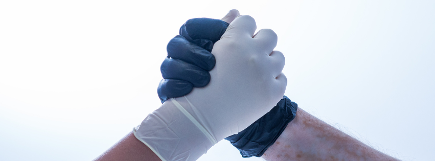 Two people, one wearing a white glove and the other wearing a blue glove, grasping hands.
