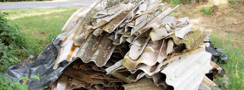 A pile of shingles containing asbestos sitting in the grass next to a road.