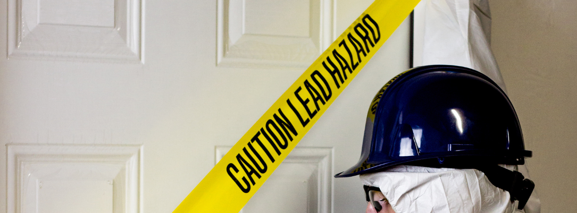 An MP Environmental Services employee wearing PPE is standing in front of a door with caution lead hazard tape over it.