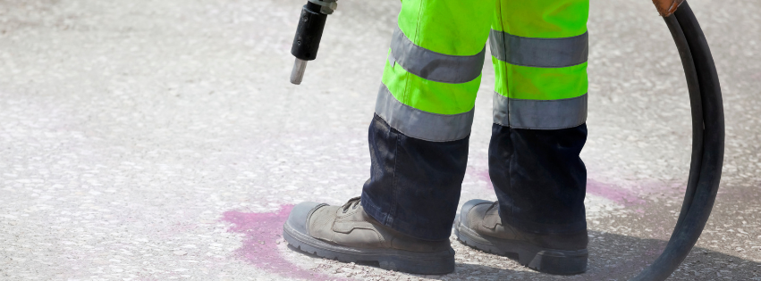 A worker dressed in protective equipment, using a hose and sprayer for dry ice blasting, to remove debris from a flooring area.