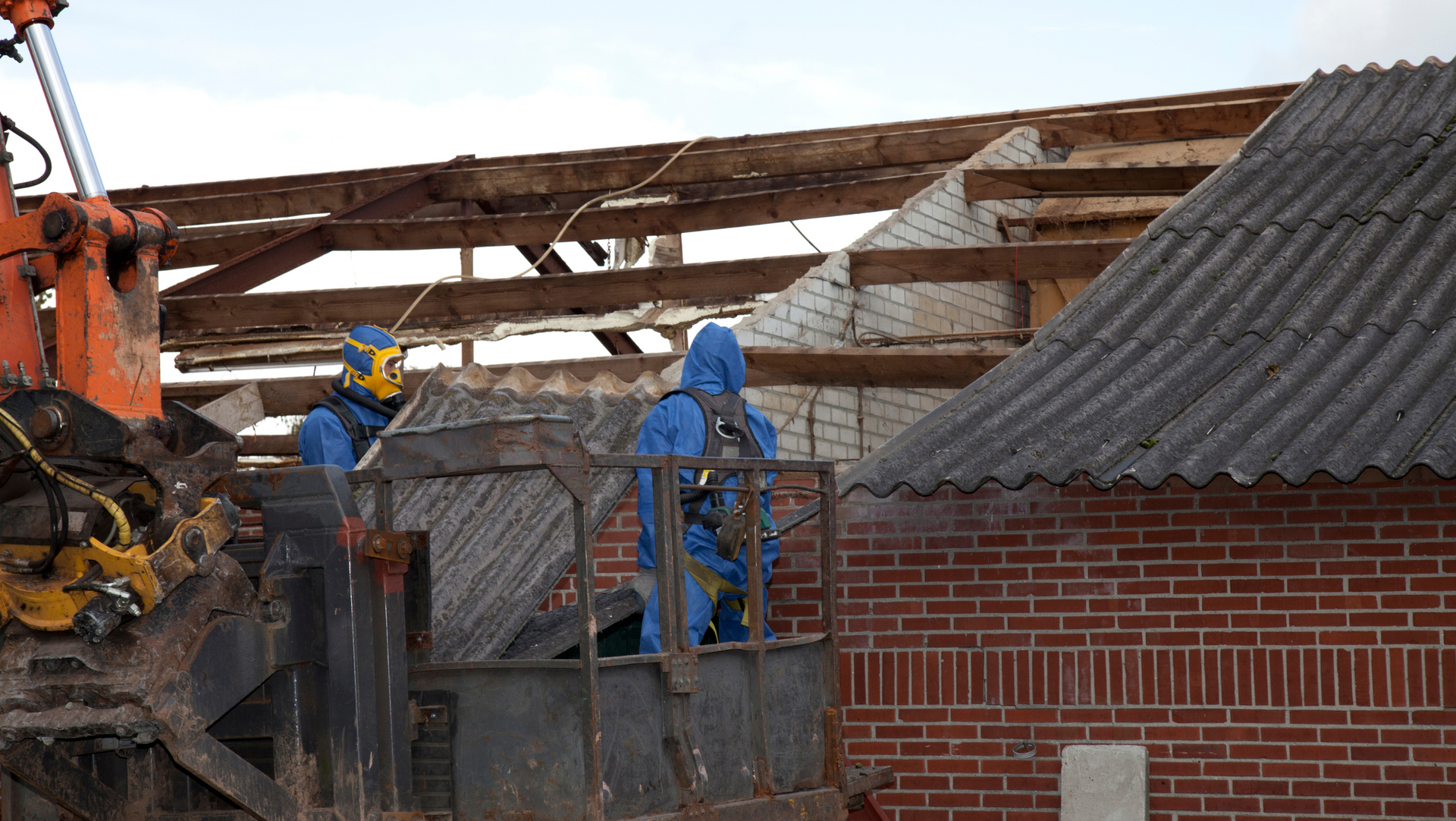 Two MP Environmental employees in protective suits are working on the roof of a brick building.