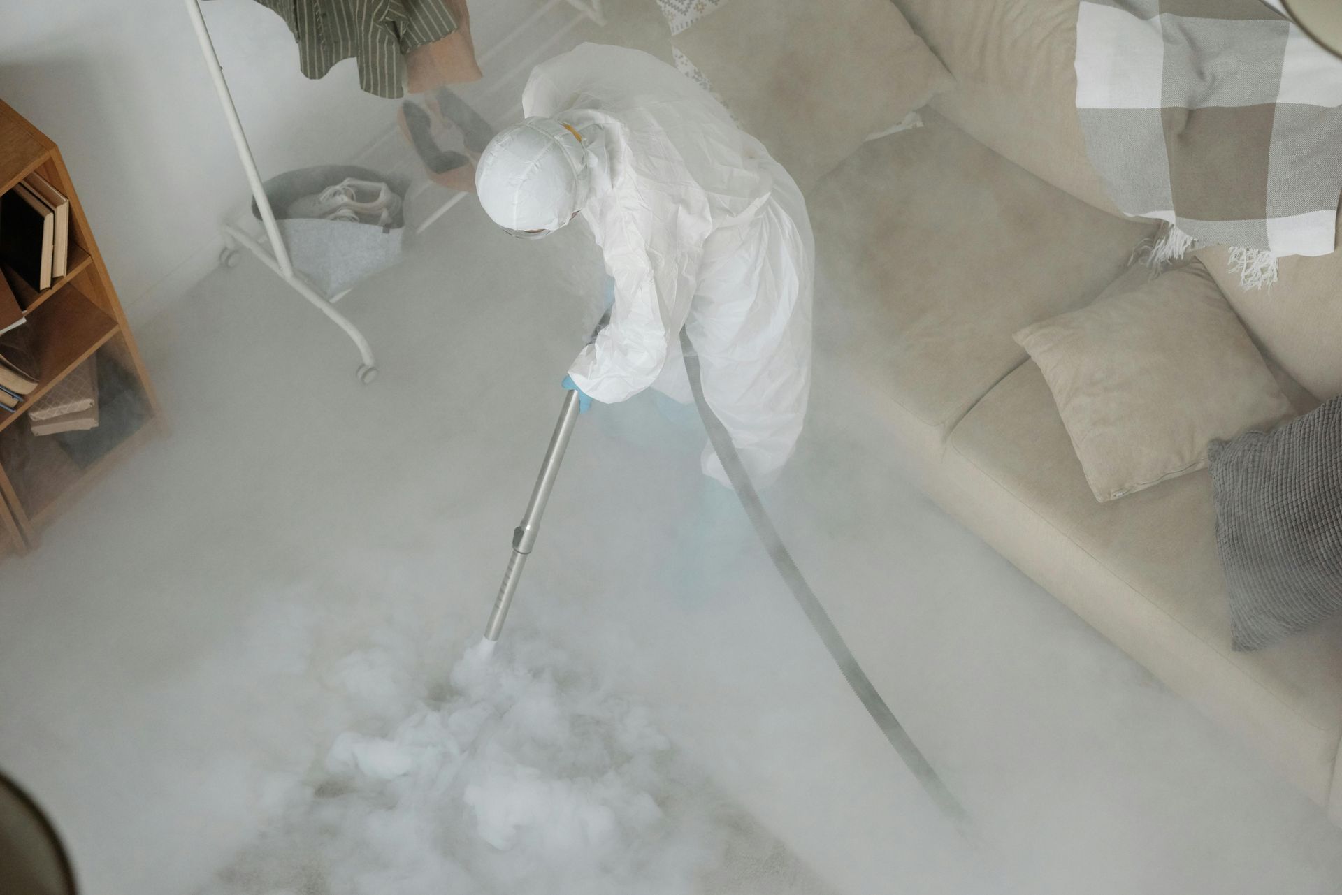 A person in a protective suit uses a dry ice cleaning machine to clean the floor of a room.